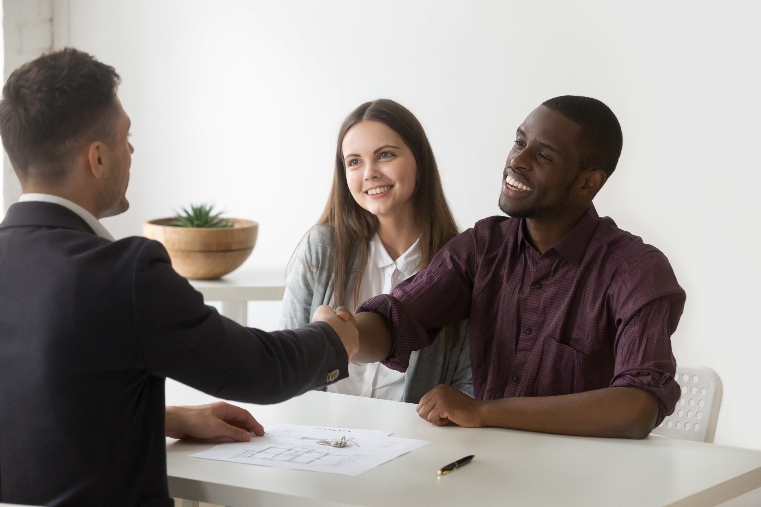 Happy satisfied interracial couple and realtor shaking hands making real estate deal
